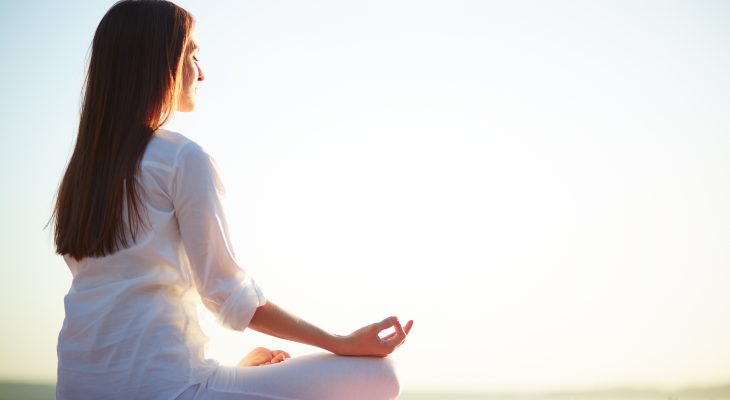 Side view of meditating woman sitting in pose of lotus against clear sky outdoors